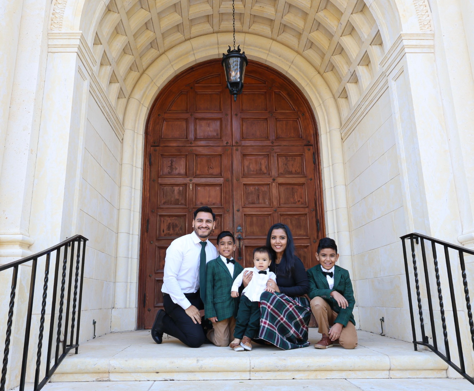 Eddie with his wife and three sons on the steps of an arched cathedral doorway.
