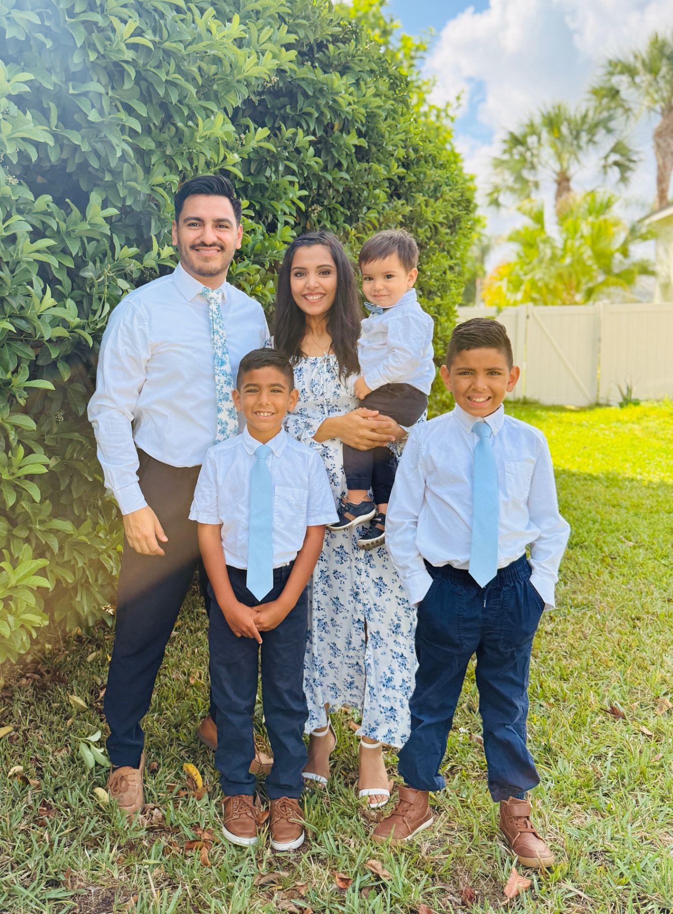 Eddie with his wife and three sons in coordinated blue and white, smiling in the backyard.