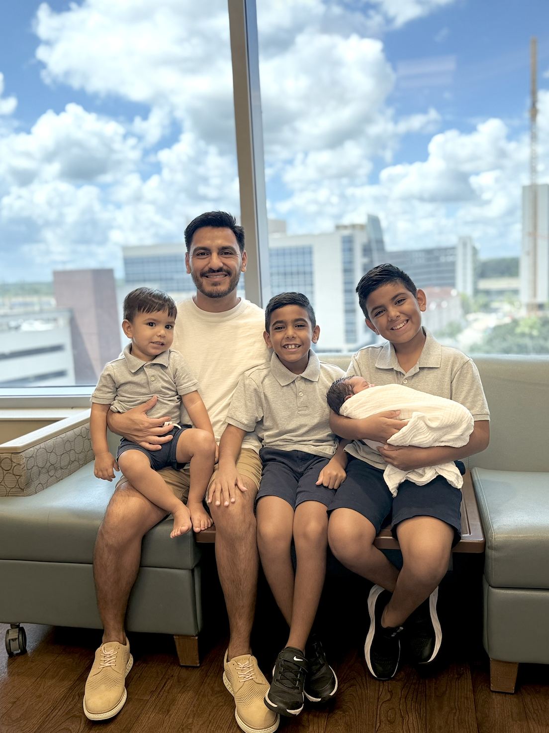 Eddie sitting by a window with his four sons, the oldest holding the newborn.