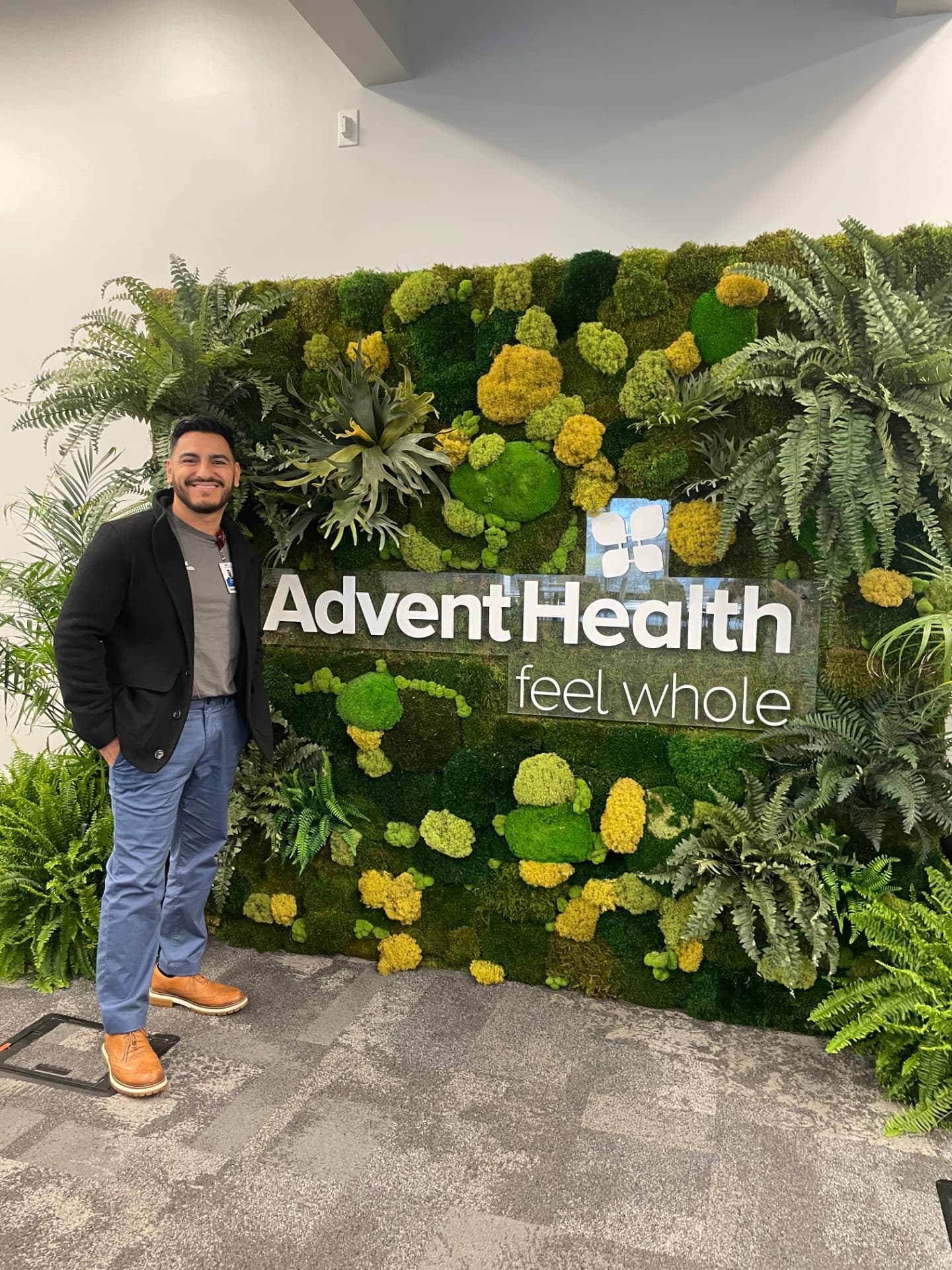 Eddie standing beside the AdventHealth 'feel whole' sign on a living moss wall.